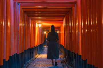 Solitary Wanderer in Traditional Japanese Torii Gates Tunnel at Dusk