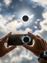 Close-up of hands holding mobile phone and taking pictures of solar eclipse - obrazy, fototapety, plakaty