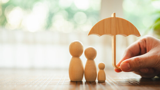 Parent and child model holding an umbrella on a wooden table, concept of health insurance, life and savings insurance