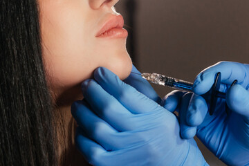 Closeup of young woman receiving injection in beauty salon. Cosmetology. Filler injection chin make...