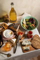 Assorted cheese, jam, honey and sliced bread. Cheese platter on the table covered with linen tablecloth. Side view.