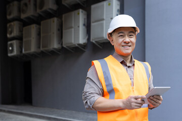 Portrait of a smiling young male construction worker in a hard hat and vest holding a tablet in his hands and looking at the camera - Powered by Adobe