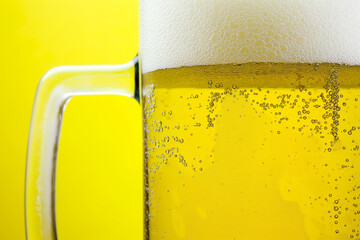A close-up of a mug of beer with a white head and small bubbles on the surface against a yellow background