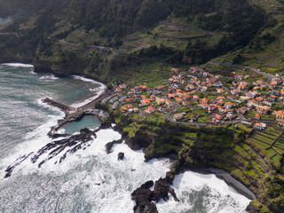 Aerial view of Seixal, a little village by the ocean with waves and surrounded with incredible mountains on the island of Madeira, Portugal.