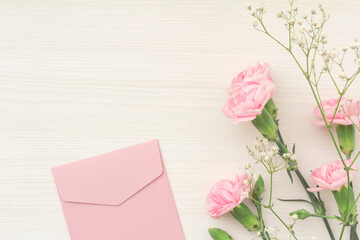 Pretty frame of pink carnations, white hazel and pink envelopes on a white wood table