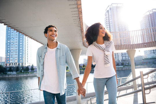 Photo of positive lovely good mood partners young funny couple soulmates holding hands together stroll outdoors enjoying city views