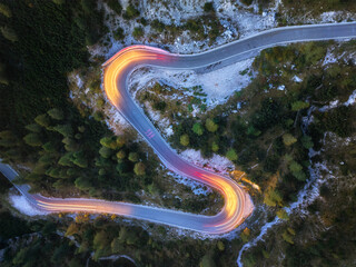 A perpendicular, unusual view of a winding road with traces of passing car lights. Long-Exposure Photography. Yellow and red lines, evening view, mountain road in the Dolomites. 