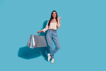 Full size photo of speechless woman dressed silk shirt holding shopping bags raising palm up staring isolated on blue color background