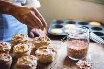 Hand adding sprinkles to chocolate cupcake food photography recipe idea - obrazy, fototapety, plakaty