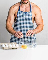 Protein food concept. Chef bodybuilder in protective apron cook eggs on kitchen table. Muscular man cooking. Healthy food and dieting. Food additives for sportsman, daily protein and calorie.
