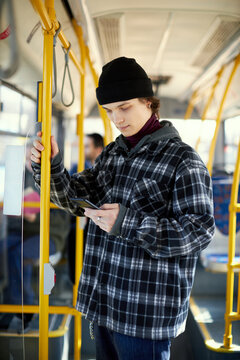 Young man in checkered shirt standing in modern tram, bus and looking on mobile phone. Convenient and cheap way of transportation. Concept of public transport, urban lifestyle