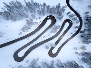Winter in the mountains: perpendicular view of a mountain road forming loops. Snow-covered trees and surroundings. Italy, Dolomites, road to Passo Rolle pass.