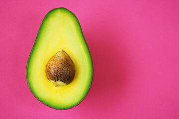 Half of a cut avocado on a pink background