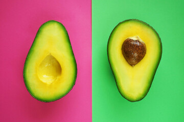 Halves of cut avocado on pink and green background