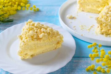 Traditional Italian Mimosa Cake, a popular Italian spring cake with sponge cake and Diplomat cream, light blue background and Mimosa Flours on a table