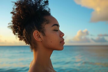 Young woman enjoying a serene moment by the ocean at sunset with a gentle breeze in her hair.