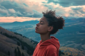 Young woman in a red hoodie finding peace amid mountainous landscape at dusk