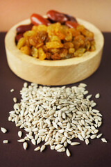 Dried dates and raisins in a wooden plate next to a sunflower seeds on a beige-brown background