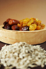 Dried dates and raisins in a wooden plate next to a sunflower seeds on a beige-brown background