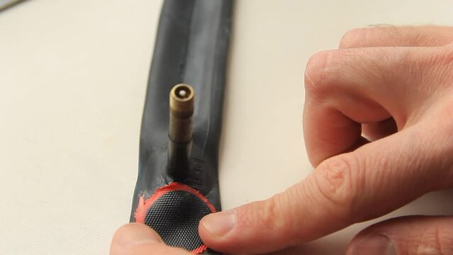 A man's hand sticks a bicycle patch on a bicycle tube