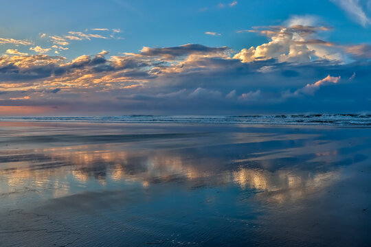 Early morning image of clouds and sky reflecting off the wet beach and shallow water at low tide.