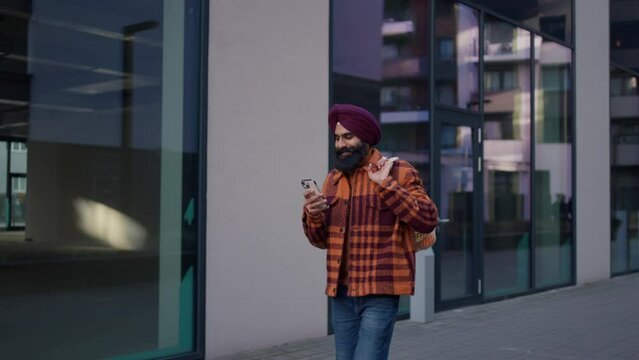 Young Indian man holding smartphone on city street. Video of handsome Indian man with turban, text messaging.