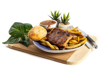 A dinner of half rack of BBQ baby back pork ribs with French fries, dinner roll and sauce on a blue plate isolated on white