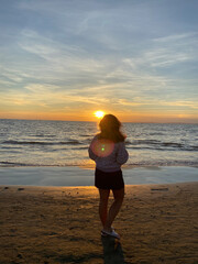Jeune femme à la plage admirant le coucher de soleil et la mer