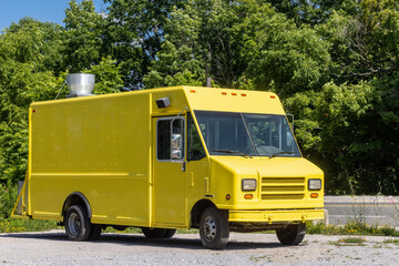 A generic yellow food truck with exhaust vent on teh roof in front of green trees