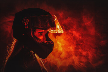 Young beautiful girl in the motorbike helmet on the fire smoke background. Street racing concept.