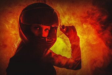 Young beautiful girl in the motorbike helmet on the fire smoke background. Street racing concept.