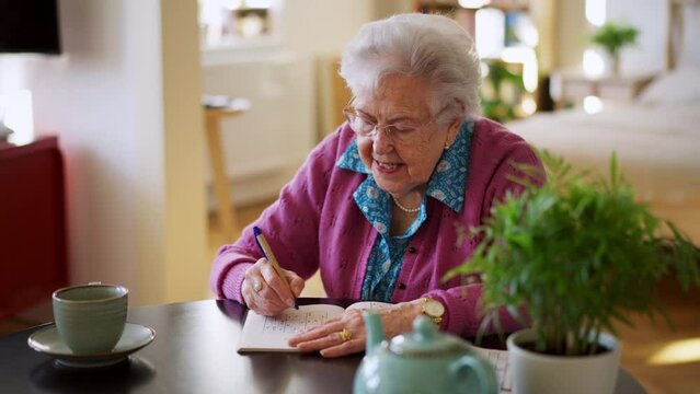 Video of elderly woman solving sudoku puzzles at home, sitting in living room. Sudoku as popular game for aging people, logical thinking, problem solving.