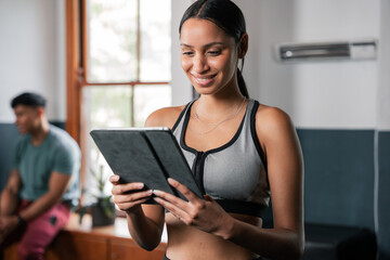 A woman smiles as she uses a tablet computer in the gym