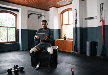 Man with prosthetic leg sits on gym bench, looks at tablet