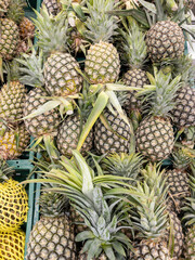 A ripe yellow pineapple with spiky green leaves sits in a market stall.