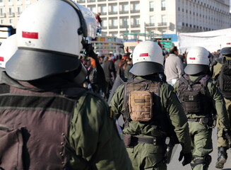Armed policemen in white helmets on public street demonstration, in background group of protesters in soft focus