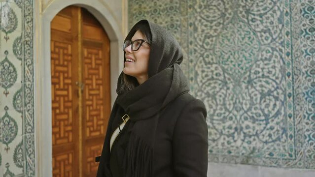A smiling woman wearing glasses and a scarf explores the ornate interior of istanbul's historical topkapi palace.