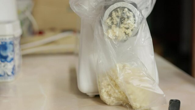 horseradish pieces collecting in a plastic bag out of a meat grinder while preparing a food or cure