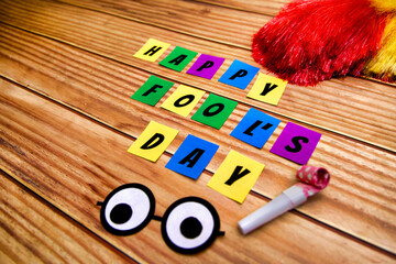 Happy Fools Day text on colorful sticky notes with accessories on wooden background