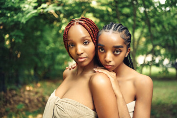 Fashion Close up outdoor portrait Beautiful young African American female couple with braids hair posing at sunny summer day green foliage. Cosmetology, perfect skin care, spa. Natural face treatment