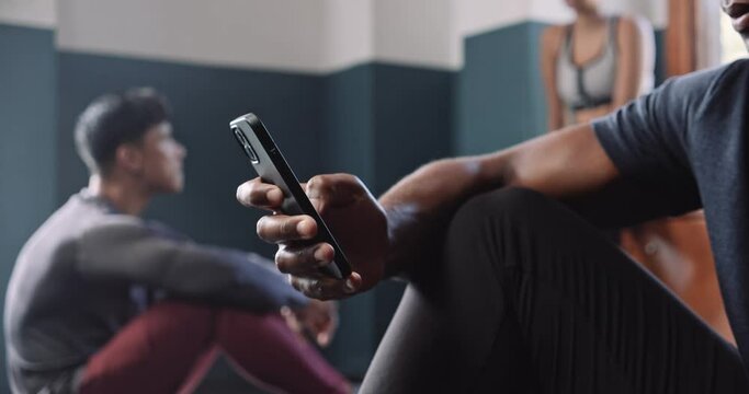 Medium shot of African athlete scrolling on mobile phone in fitness studio 