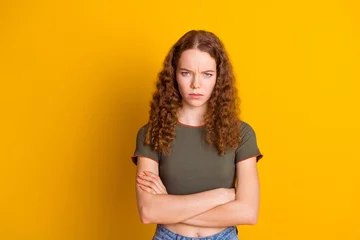 Deurstickers Photo of serious angry unsatisfied woman standing with crossed hands problem trouble conflict fight isolated on yellow color background © deagreez
