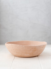 An empty beige handmade clay dish in sunny shadows on a light gray background. A minimalistic concept for the design of a modern interior.