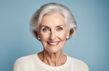 Portrait of a stylish cute elderly woman on a blue monotone background. A beautiful well-groomed elderly woman is smiling, wearing a white sweater. Healthy lifestyle concept for elderly women