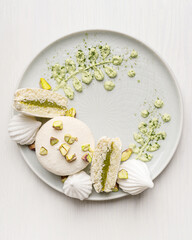 Top view of restaurant plating or decoration of dessert made with crunchy sweet macaron or french macaroon with pistachio flavour filling, meringue, crushed nuts and green cream cheese on plate