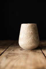 An empty old clay vase with a rough texture on an old wooden table. Hard shadows. Dark tones. Front...