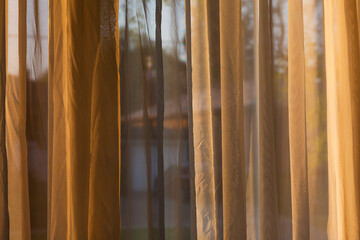 Brown transparent hanging curtain by large window with view to the outside neighbourhood at sunset
