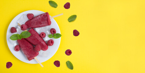 Popsicles with raspberry on the white plate on the yellow background. Copy space. Top view.