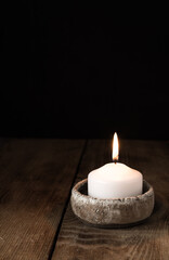 One lit candle stands on a wooden table on a dark background