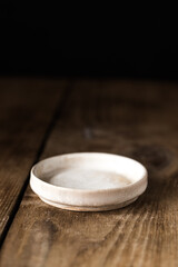 an empty round ceramic plate on a wooden table. Dark background. Vertical orientation.